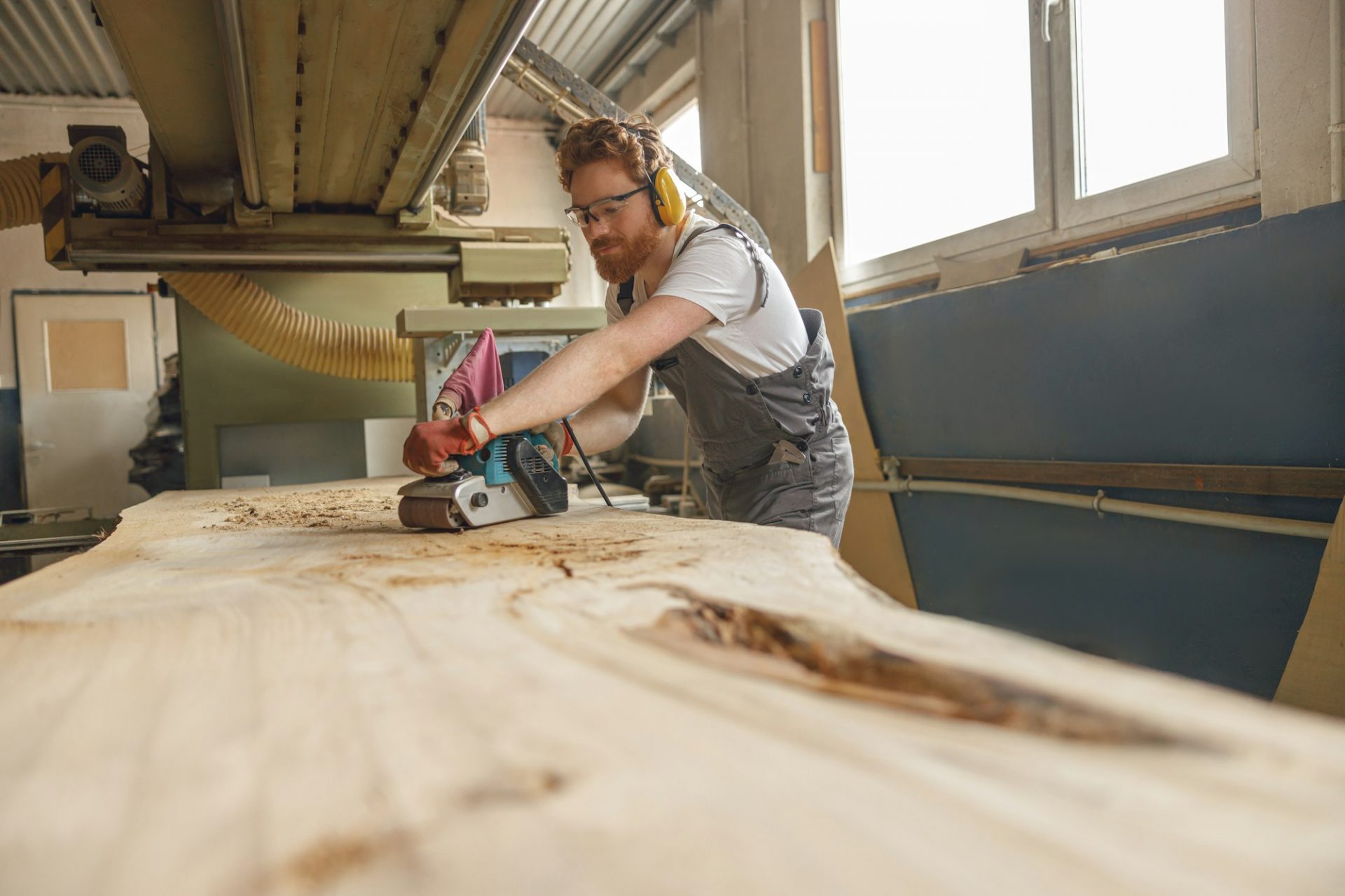 Bearded male wood worker using electric sander for wood. Carpentry workshop. High quality photo