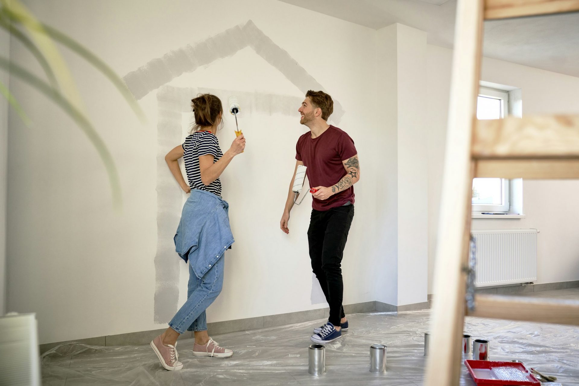 Young caucasian couple painting house shape on wall in new house